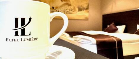 A hotel room with a bed, a pillow, a cup, and a plate on a table.