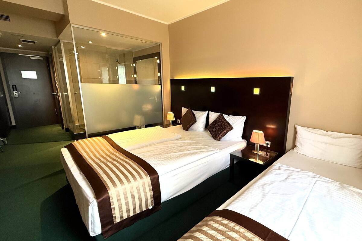 A hotel room with two beds, a glass shower enclosure, and a mirror.