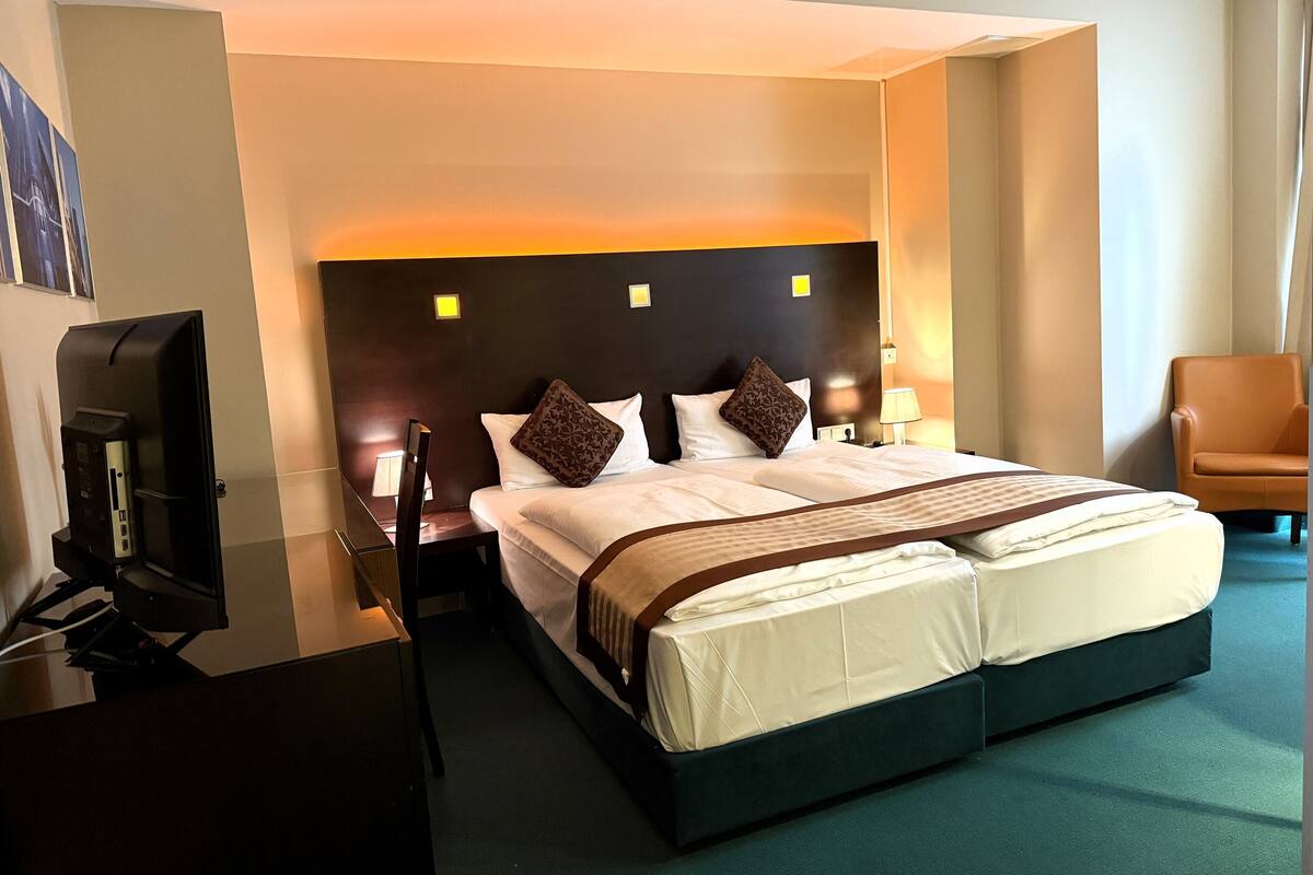 A hotel room with a large bed, a desk with a computer, a chair, and a TV.