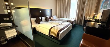 A hotel room with a large bed, a desk, a chair, a TV, and a bathroom area.