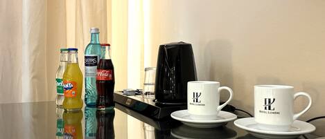 Una mesa de hotel con una cafetera, dos tazas y tres botellas de bebidas.