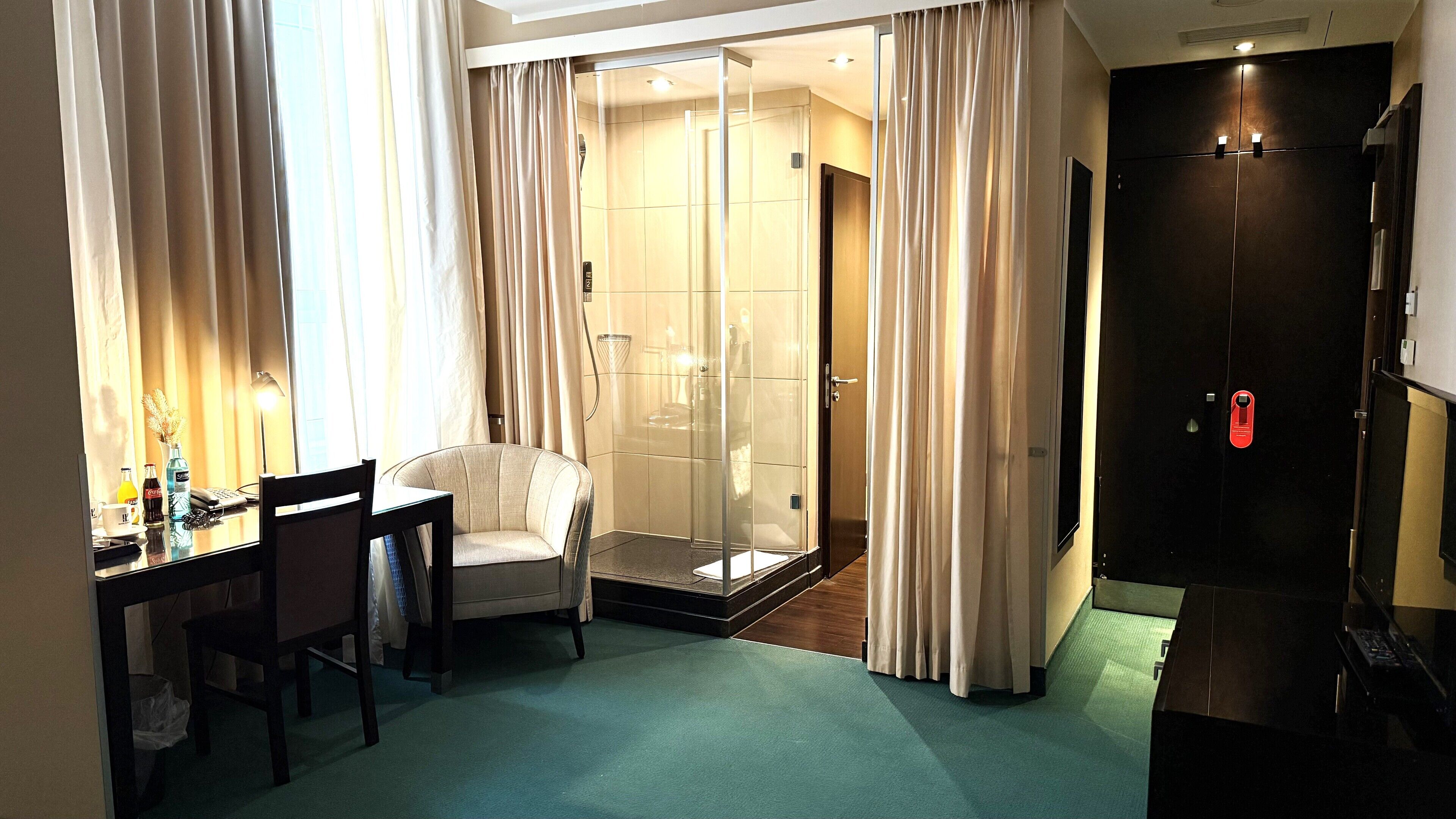 A hotel room with a desk, chair, and a shower area.