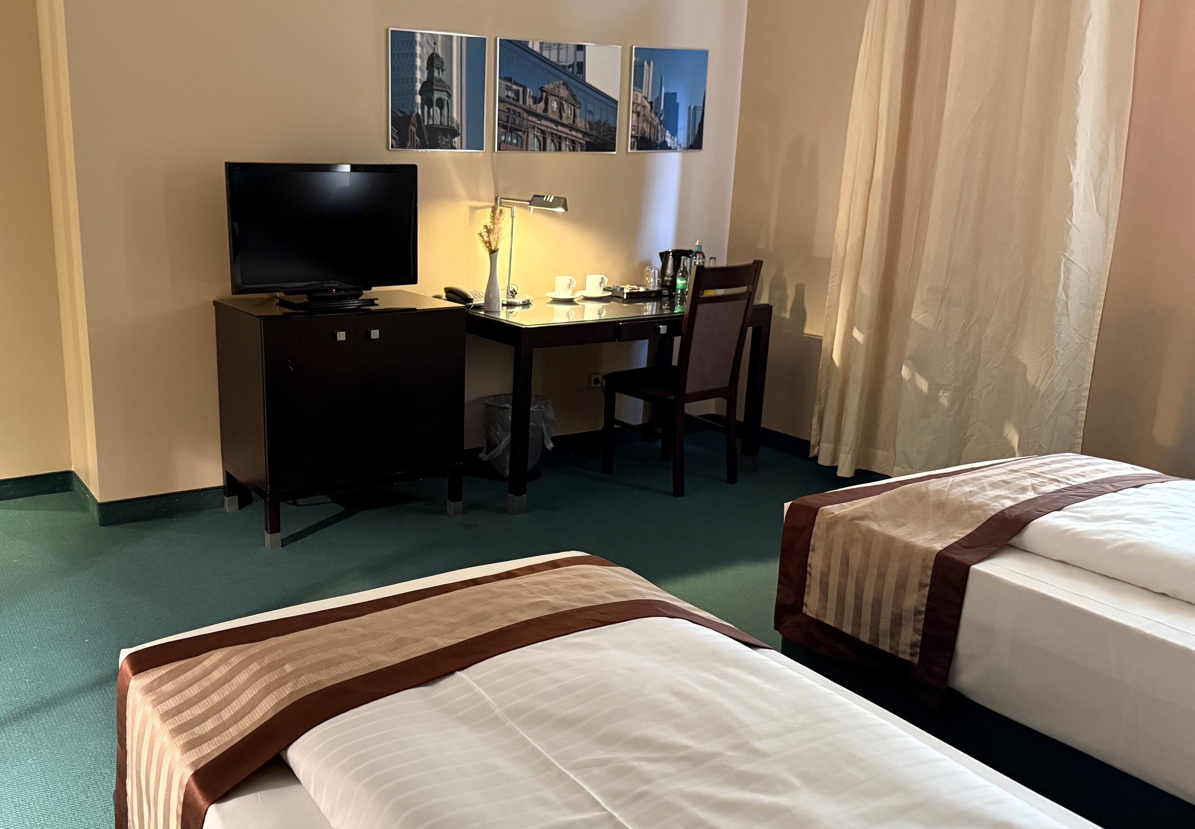 A hotel room with a bed, a desk with a computer and lamp, a chair, and a TV.
