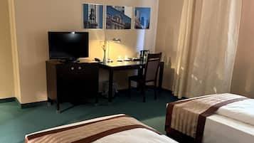Ein Hotelzimmer mit einem Bett, einem Schreibtisch mit Computer und Lampe, einem Sessel und einem Fernseher.