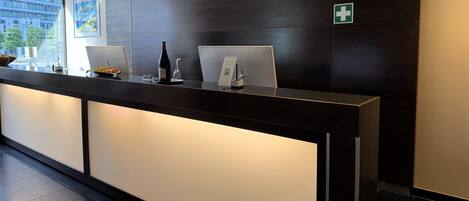 A hotel reception desk with a computer, a wine bottle, and a QR code sign.