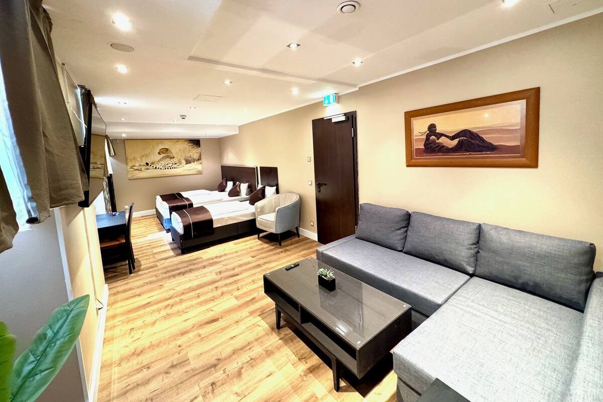 A modern hotel room with a bed, a sofa, a coffee table, and a painting on the wall.
