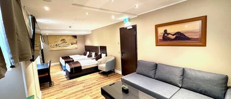 A modern hotel room with a bed, a sofa, a coffee table, and a painting on the wall.