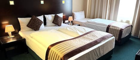 A hotel room with two beds, a nightstand with a lamp, and a window with curtains.