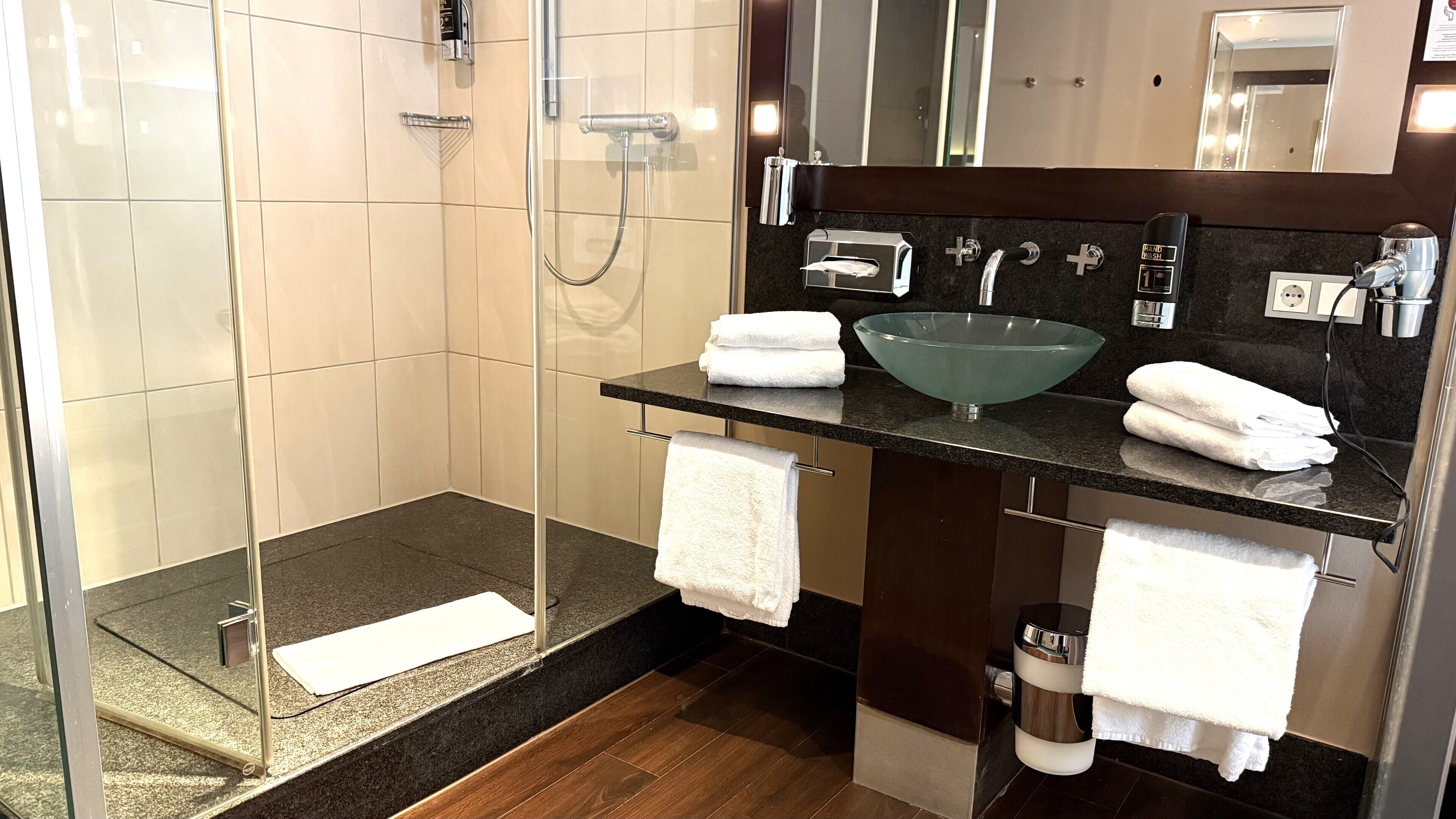 A modern bathroom with a glass shower enclosure, a glass sink, and a dark countertop.