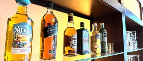 Uno scaffale con diverse bottiglie di liquori, tra cui Sierra Tropical Chilli, Johnnie Walker Black Label, Chivas Regal e Absolut Vodka.