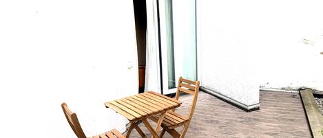 Une table en bois et deux chaises sur une terrasse en bois, avec un mur blanc en arrière-plan.