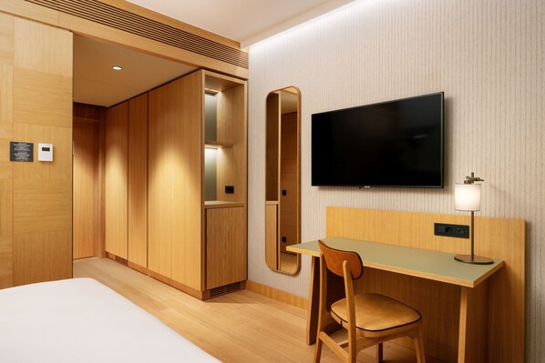 A hotel room with a bed, a desk, a chair, a TV, and a mirror.