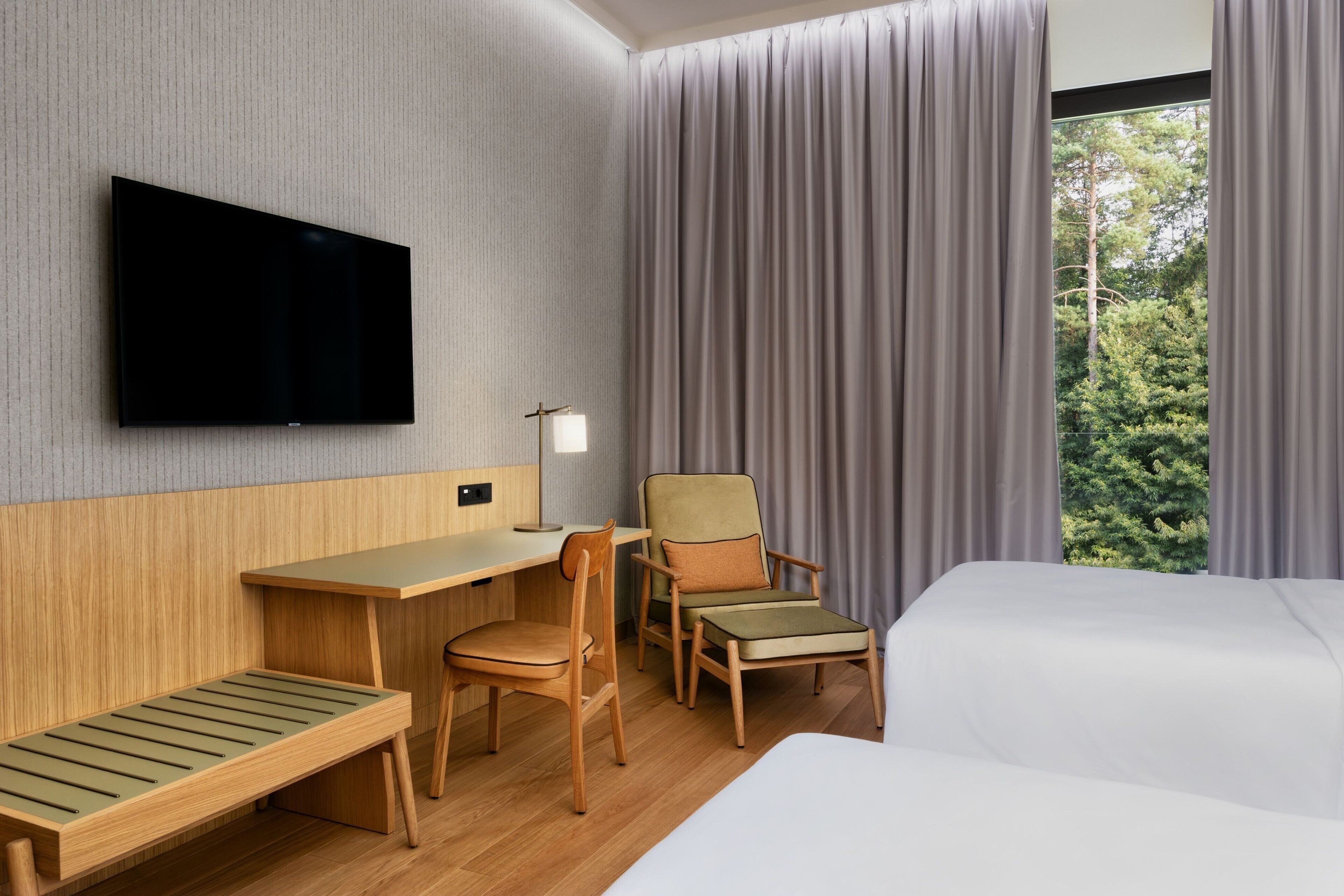 A hotel room with a bed, a desk, a chair, a TV, and a window with curtains.