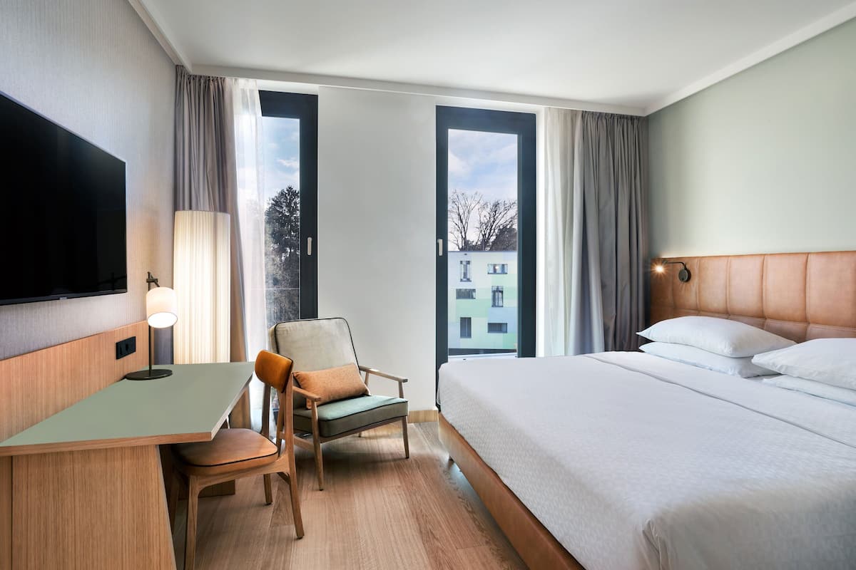 Ein Hotelzimmer mit Bett, Schreibtisch, Stuhl, Fernseher und großen Fenstern.