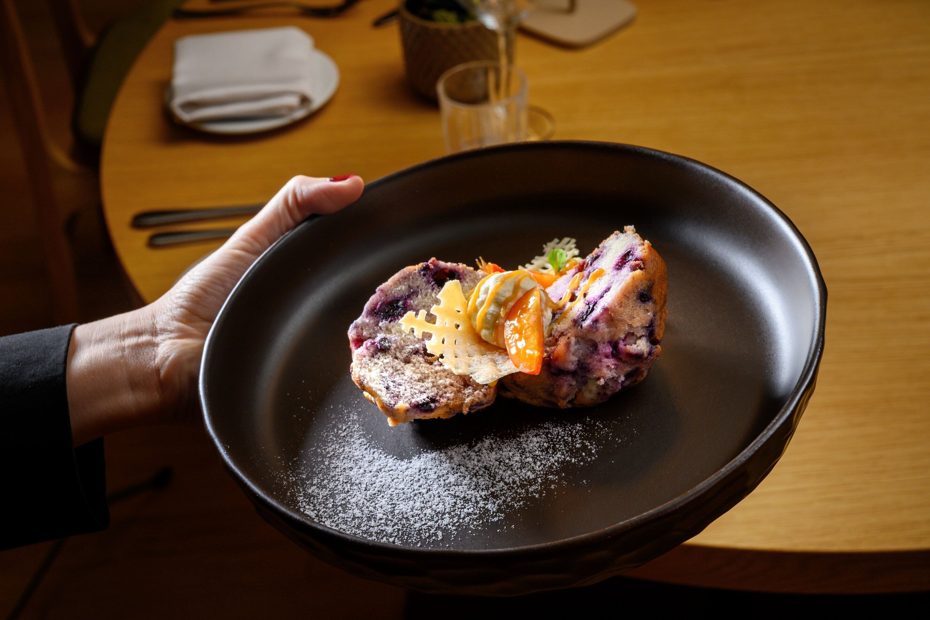 A person holding a black bowl containing a dessert with fruit and a powdered topping.