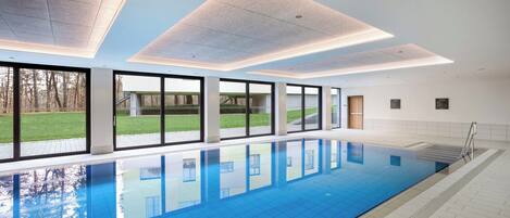 A modern indoor swimming pool with clear glass windows, a tiled floor, and a ceiling with recessed lighting.