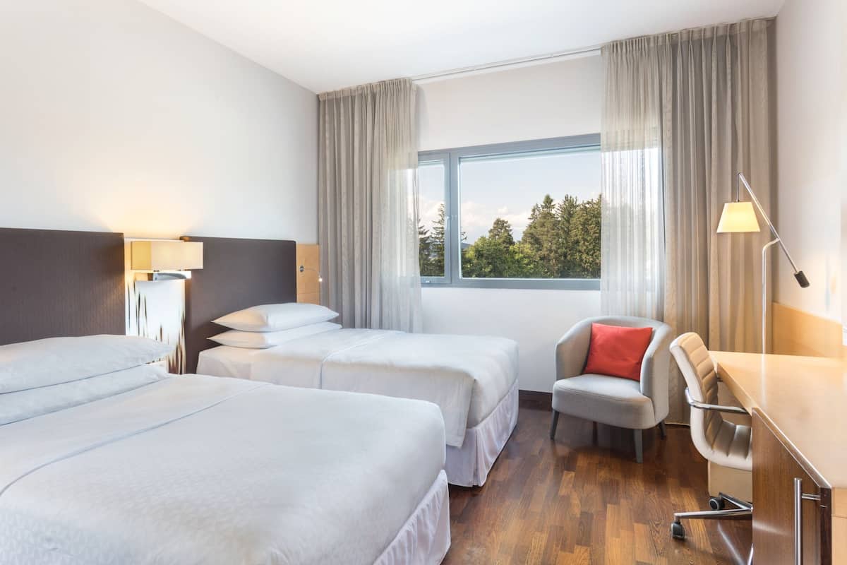 Ein Hotelzimmer mit zwei Betten, einem Schreibtisch, einem Stuhl und einem Fenster mit Vorhängen.