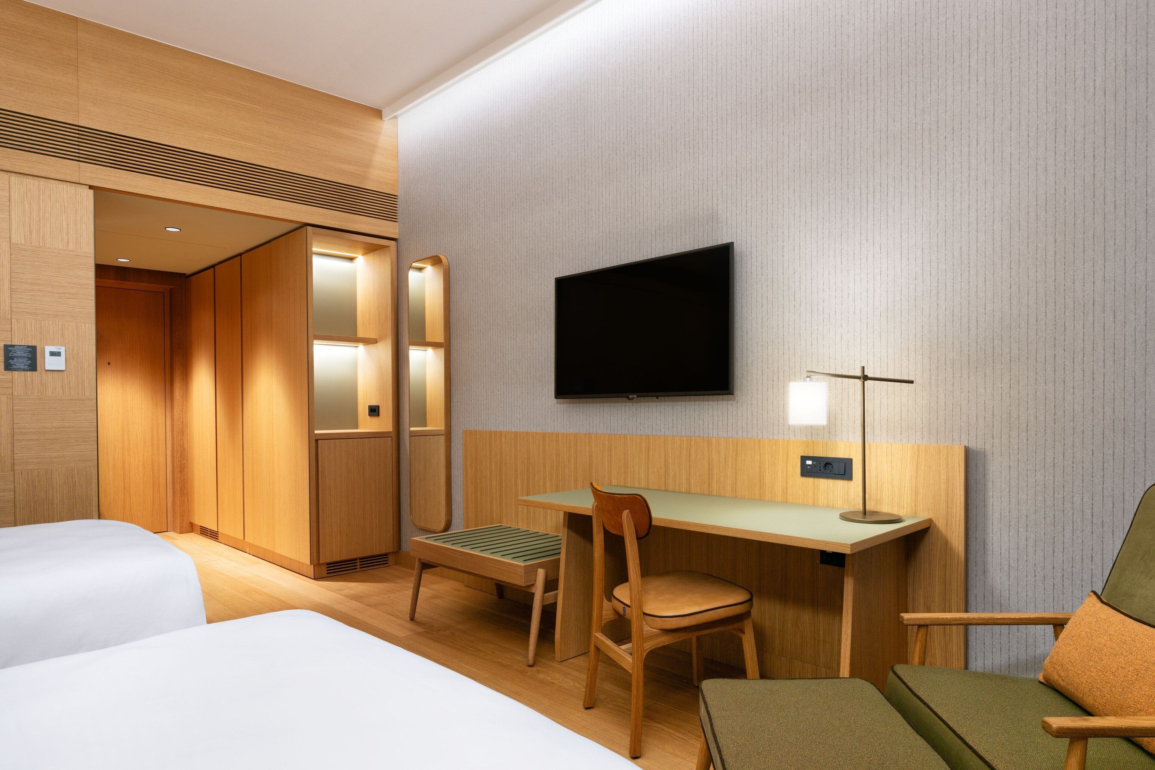 A hotel room with two beds, a desk, a chair, a television, and a lamp.