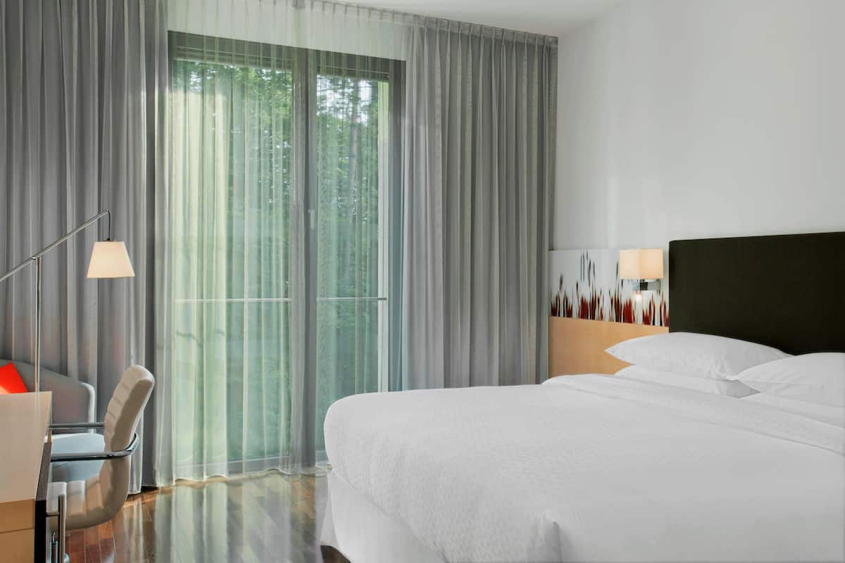 Ein modernes Hotelzimmer mit einem großen Bett, einem Schreibtisch mit Stuhl und Blick durch transparente Vorhänge.