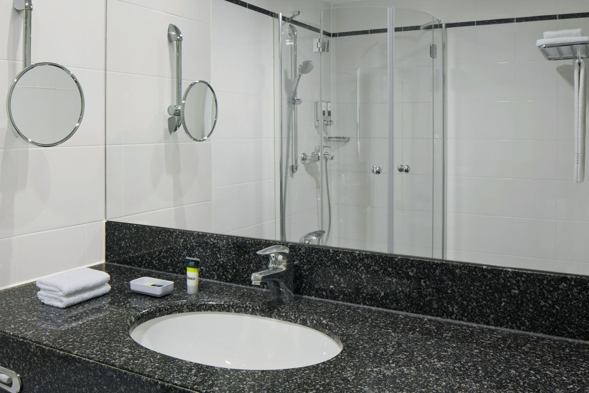 Un baño con un lavamanos blanco, encimera de granito, un espejo, ducha y toallero.