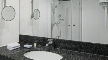 Un baño con un lavamanos blanco, encimera de granito, un espejo, ducha y toallero.