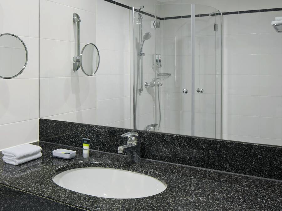 Un baño con un lavamanos blanco, encimera de granito, un espejo, ducha y toallero.