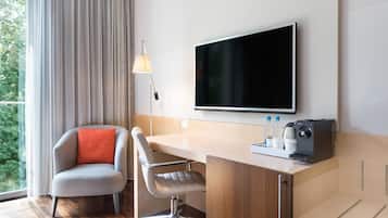 A modern hotel room with a wooden desk, two chairs, a flat-screen TV, a lamp, and a coffee machine.