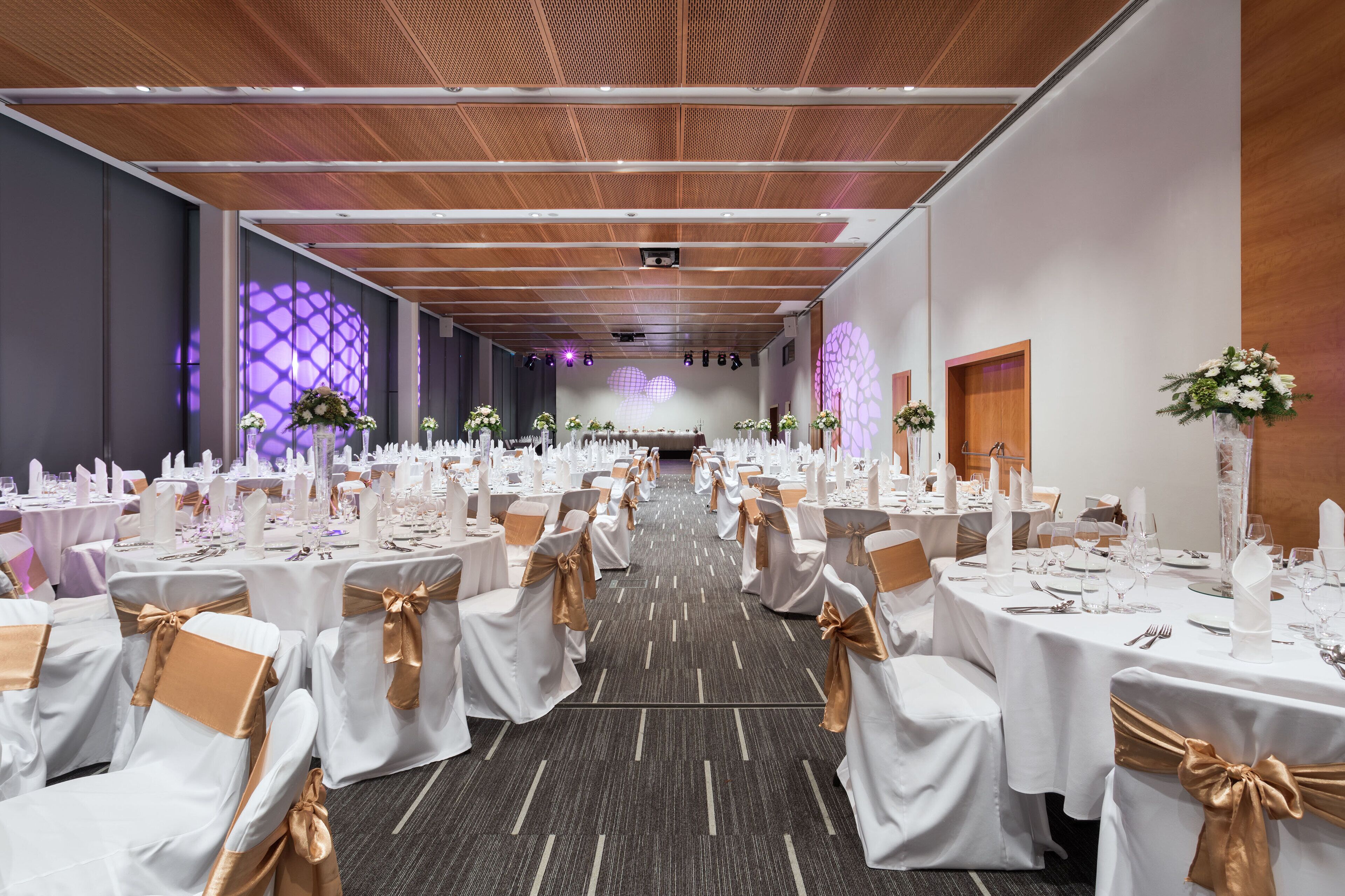 A banquet hall with rows of tables set for a formal event, featuring white tablecloths and gold sashes.