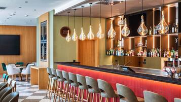 A bar area with a checkered floor, bar stools, hanging light fixtures, and a wall-mounted TV.