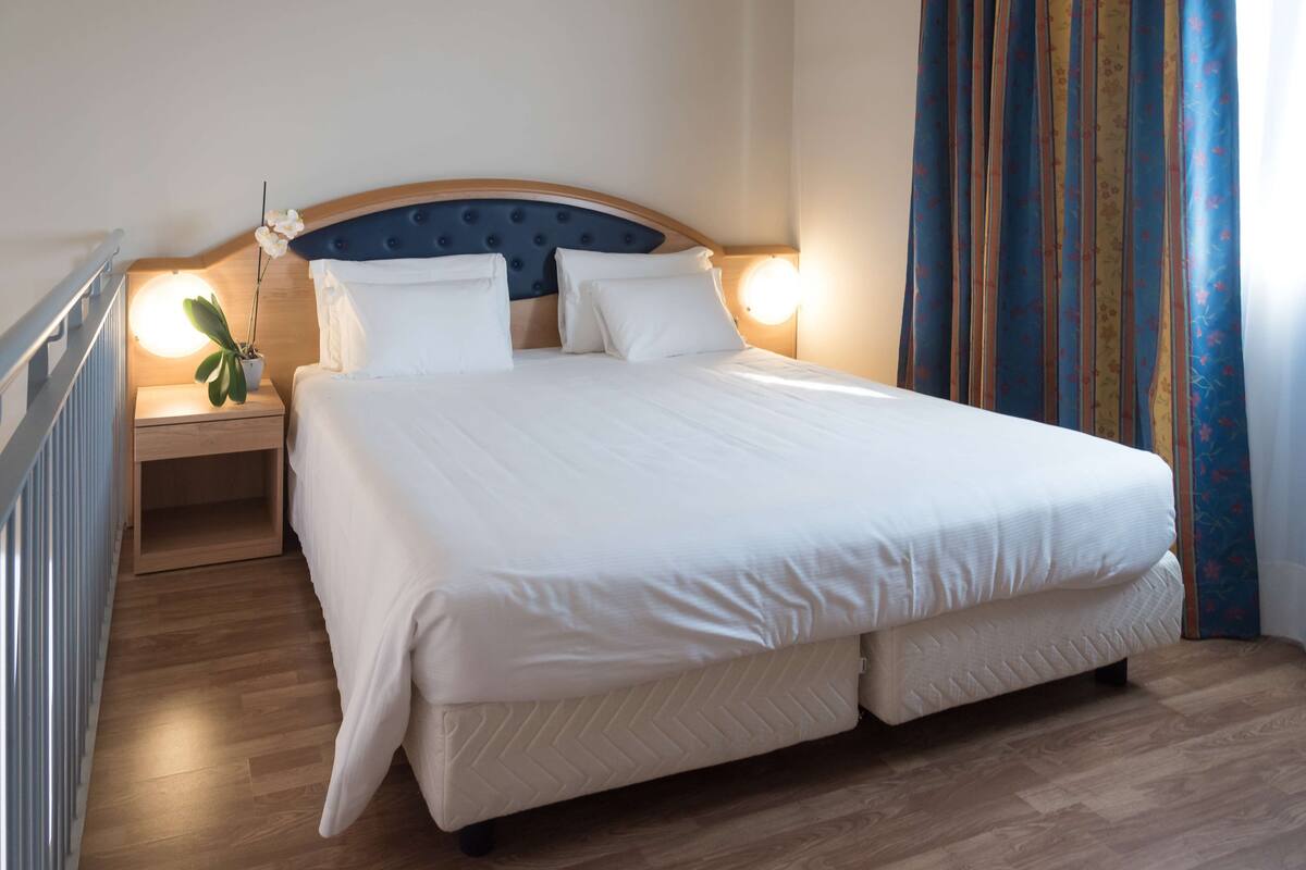 A neatly made bed with white linens, a wooden headboard, and two bedside lamps.