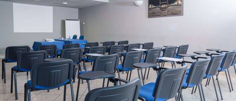 A conference room with rows of chairs and tables, a projector screen, and a whiteboard.