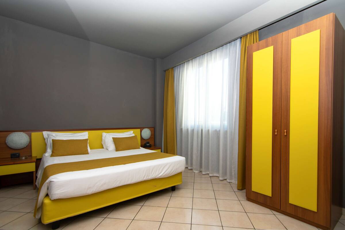 A hotel room with a bed, a wardrobe, and curtains.