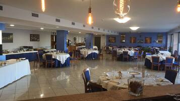 A spacious restaurant with multiple dining tables and chairs, a buffet area, and hanging pendant lights.