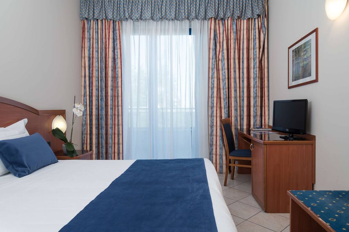 A hotel room with a bed, a desk, a chair, a television, and a framed picture on the wall.