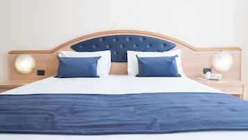 Una cama cuidadosamente hecha con cabecera azul, ropa de cama blanca y almohadas azules a juego. Hay dos lámparas de noche y un teléfono en la mesita.