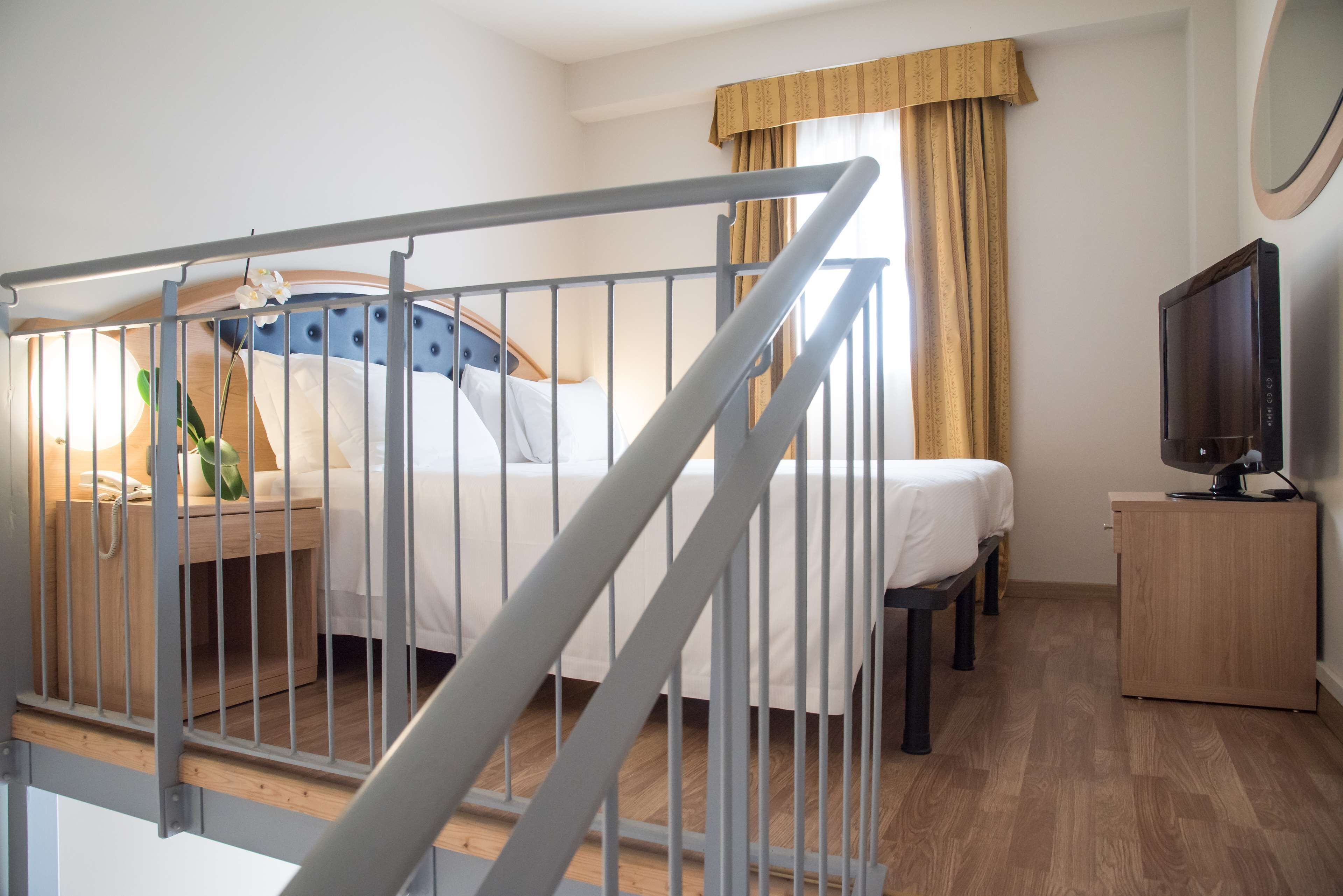 A hotel room with a bed, a bedside table with a lamp, a TV, and a wooden cabinet.