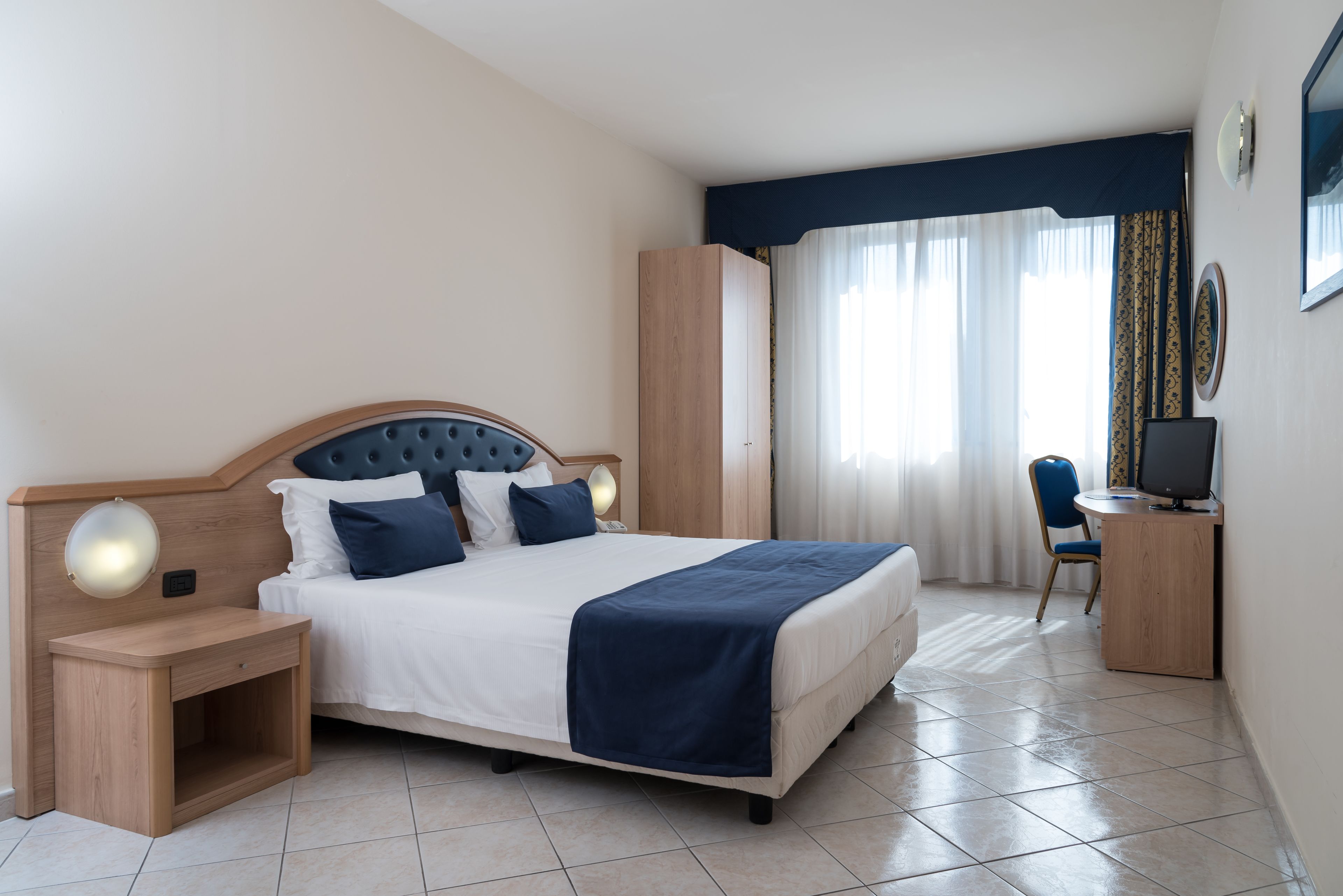 A hotel room with a bed, bedside table, desk, chair, and curtains.