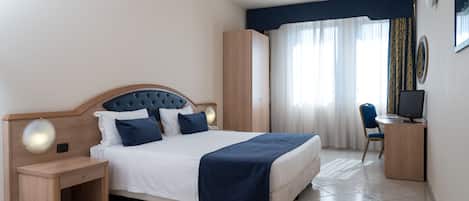 Una habitación de hotel con cama, mesita de noche, escritorio, silla y cortinas.