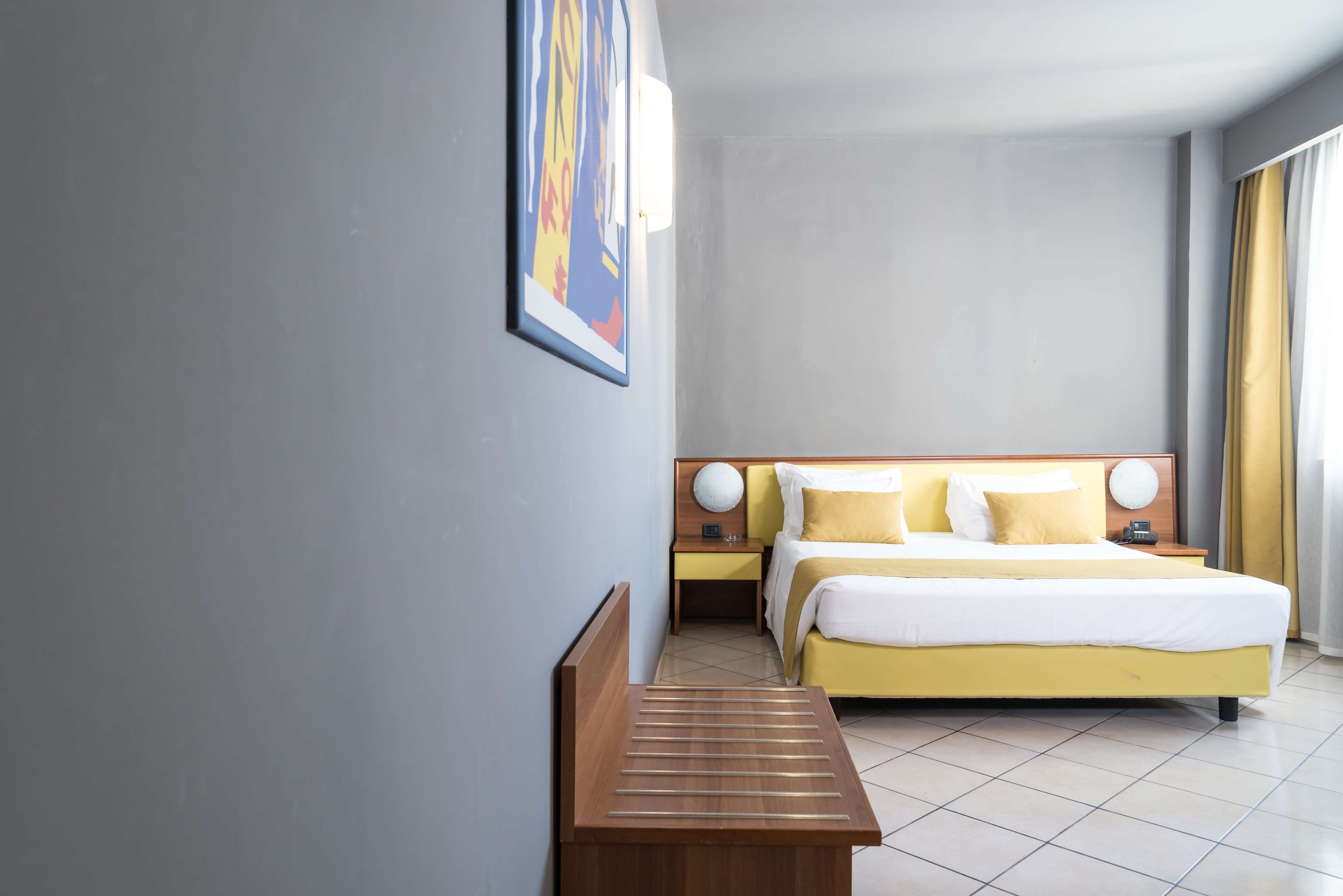 Una habitación de hotel con una cama, mesitas de noche, un banco y una obra de arte en la pared.