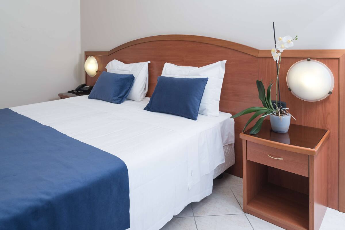 A neatly made bed with white and blue bedding, a bedside table with a lamp, and a potted orchid.