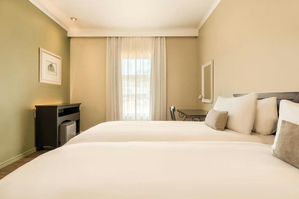 Quarto de hotel com uma cama grande, uma escrivaninha, uma cadeira e uma janela com cortinas.