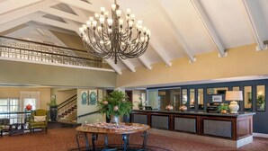 Eine geräumige Lobby mit hoher Decke, einer imposanten Chandelier, einem runden Tisch mit Stühlen, einem Empfangsbereich und einer Treppe, die in eine obere Ebene führt.