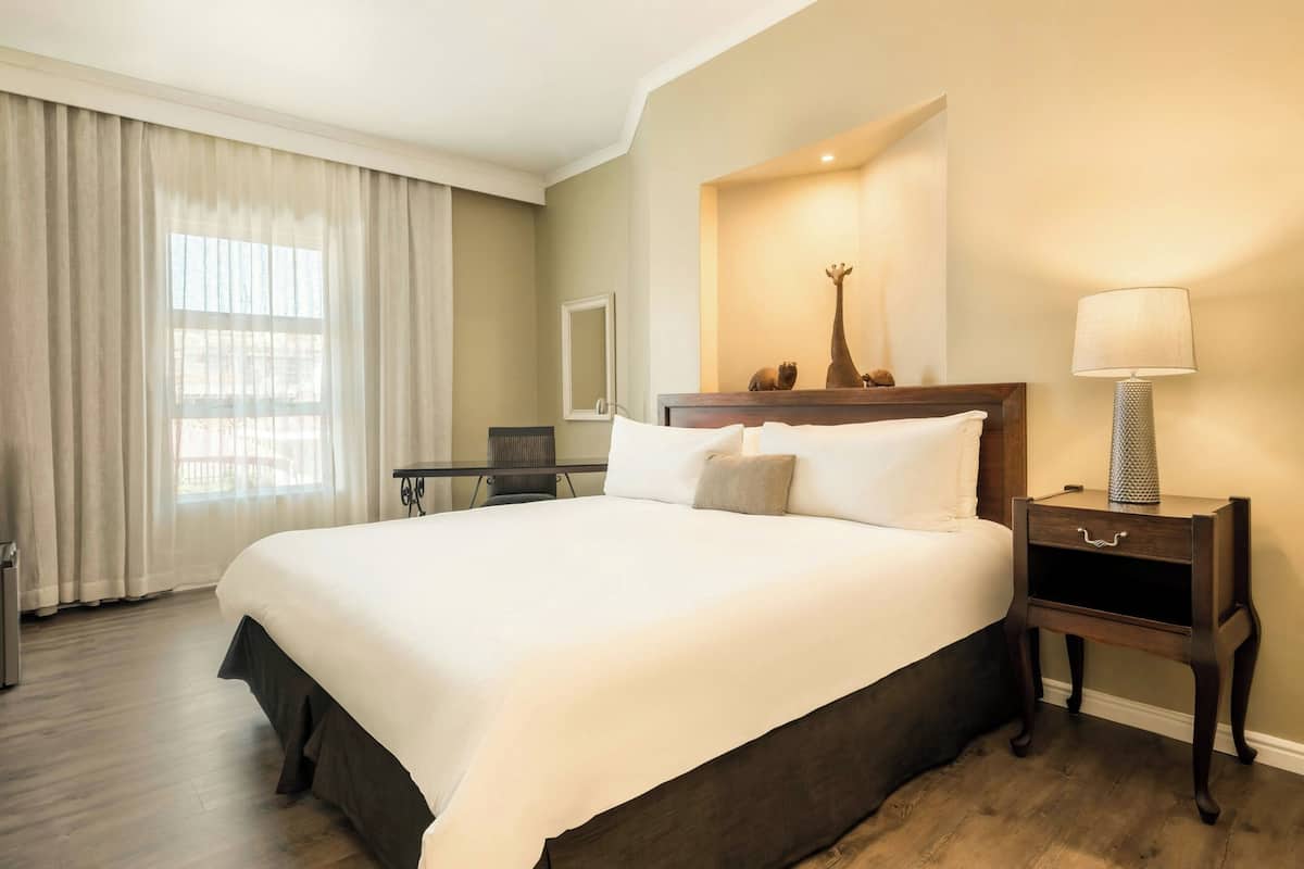 Una habitación de hotel con una cama grande, un escritorio, una silla, una lámpara y un espejo.