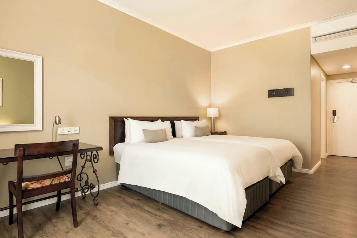 Habitación de hotel con cama, escritorio, silla, lámpara y espejo en la pared.
