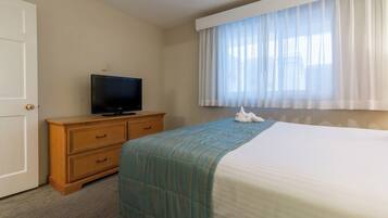 A hotel room with a bed, a TV on a wooden dresser, and a window with sheer curtains.