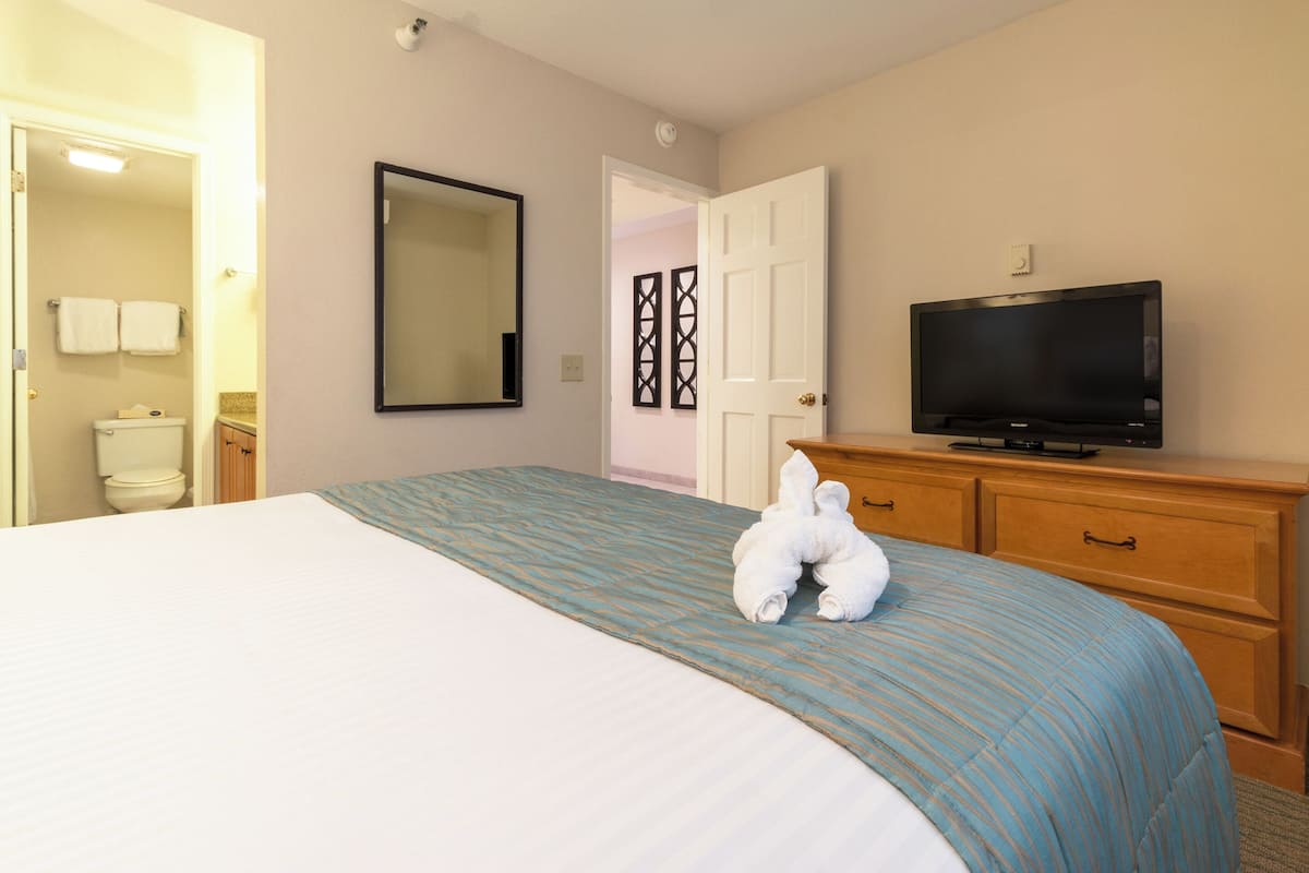 A hotel room with a bed, a television, a dresser, and a bathroom visible through an open door.