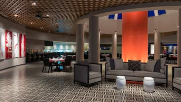 Een moderne lobby met een vloer met geometrisch patroon, een centraal zithoek met banken en fauteuils, en een grote verlichte pilaar.