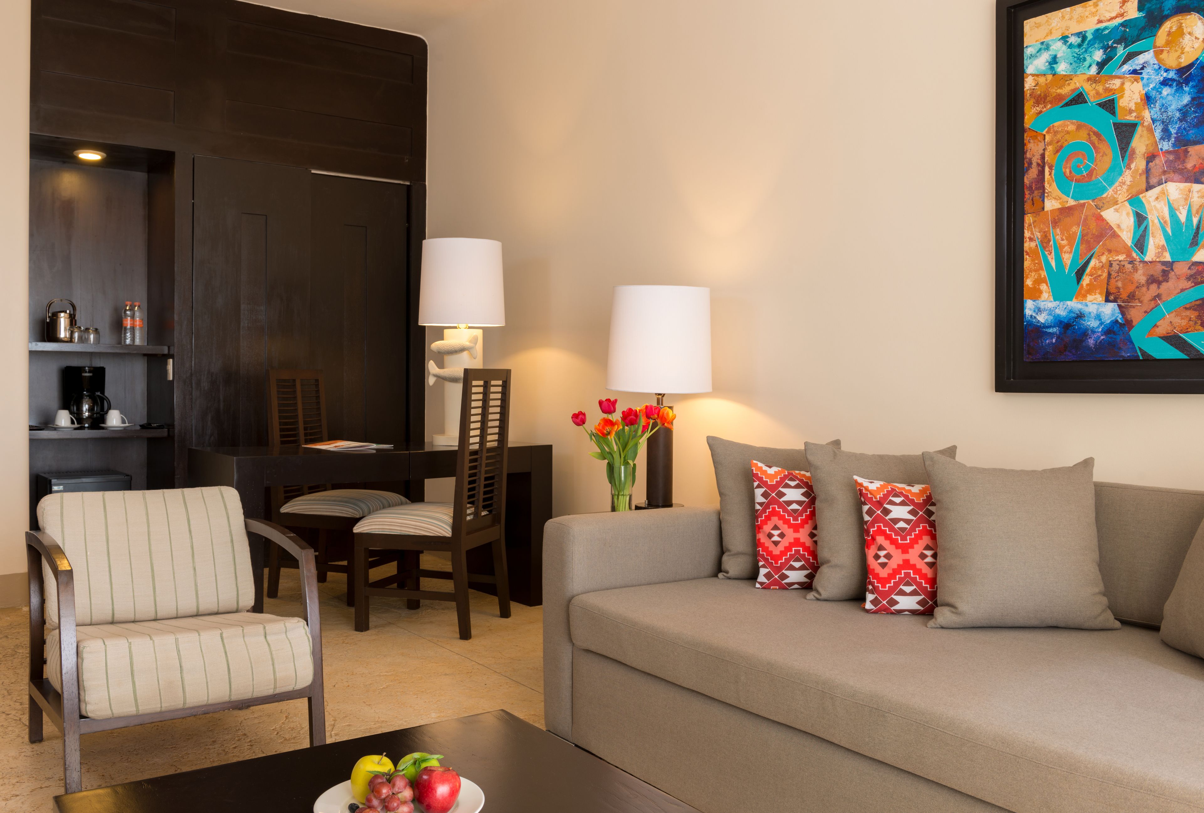 A modern living room with a sofa, armchair, dining table, and chairs. A coffee machine and a vase with flowers are on the side table.