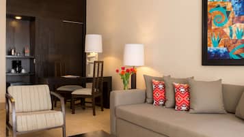 A modern living room with a sofa, armchair, dining table, and chairs. A coffee machine and a vase with flowers are on the side table.