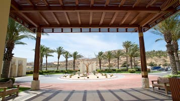 A covered outdoor area with a circular seating arrangement, palm trees, and a view of a hilly landscape.